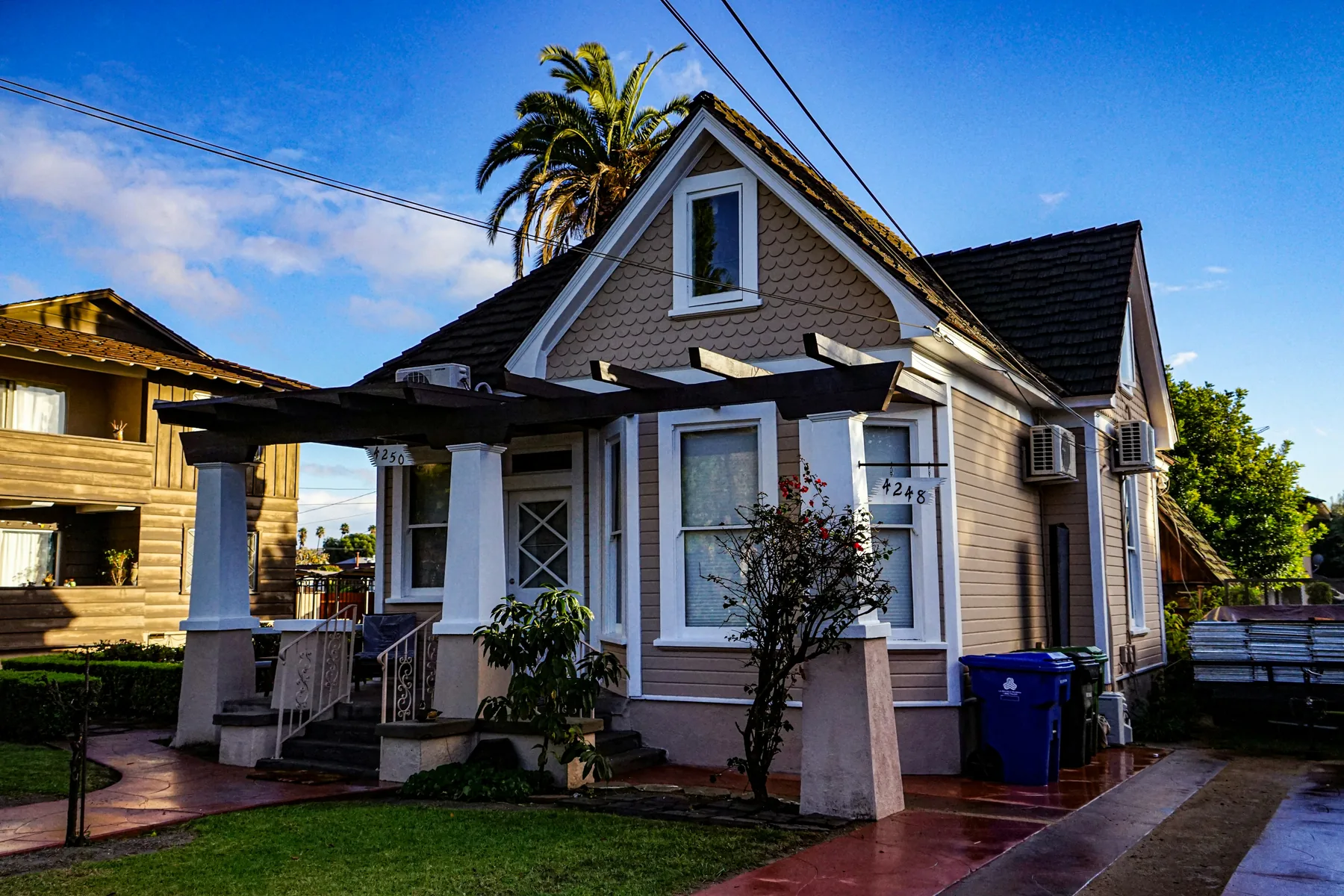 A tan bungalow with a covered porch and a palm tree behind it