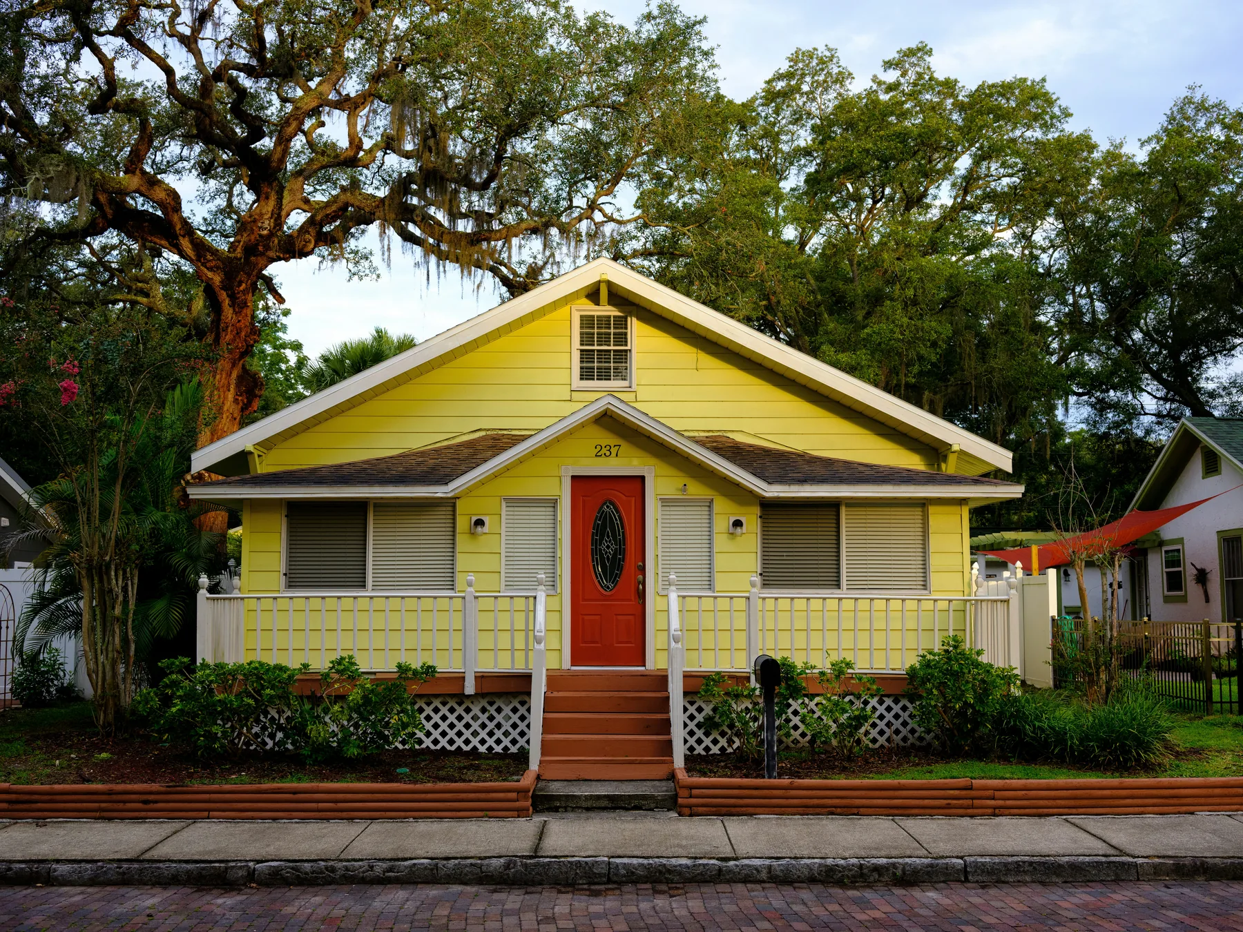 A yellow timber cottage with a red front door under a live oak