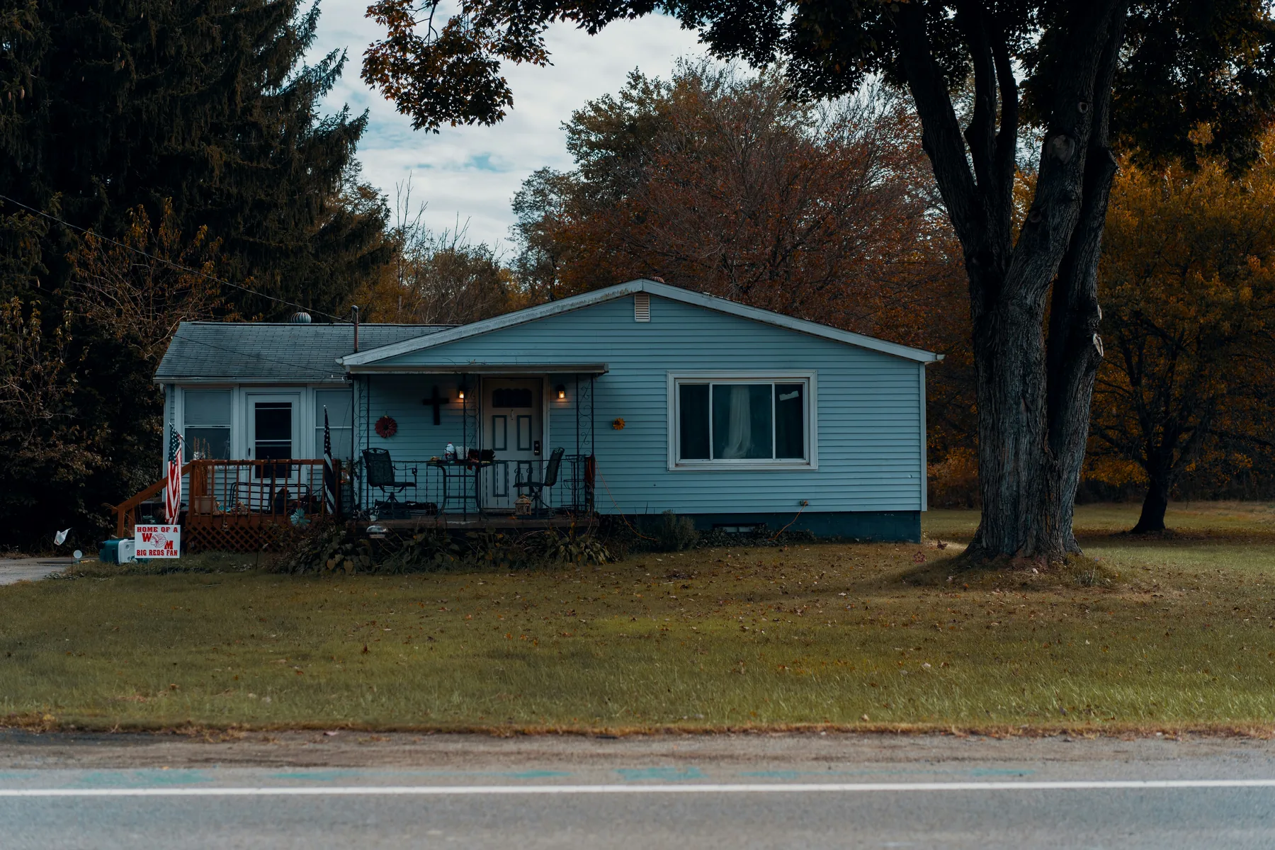 A pale blue single-storey house on a roadside lot in late autumn