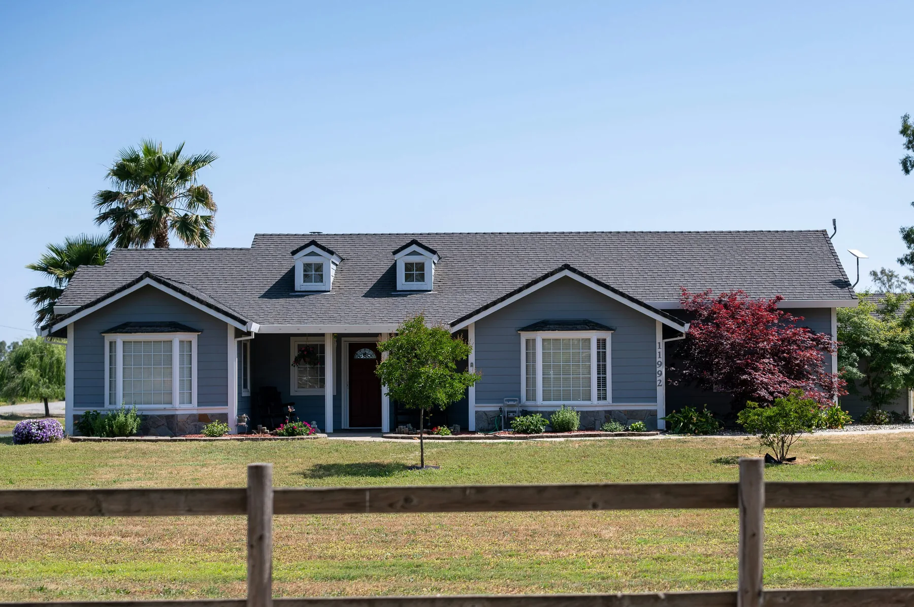 A single-storey grey ranch house behind a split-rail fence