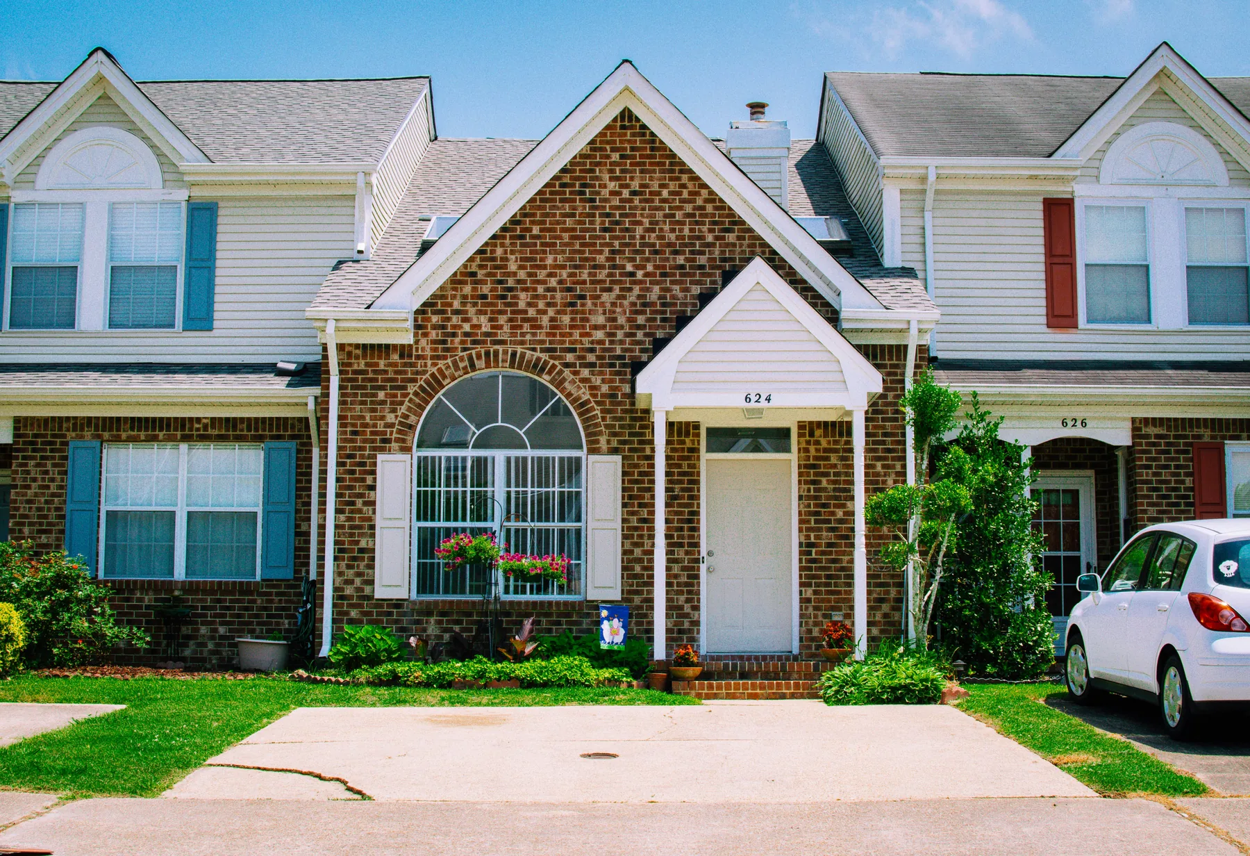 A brick townhouse in a suburban row with a car in the driveway
